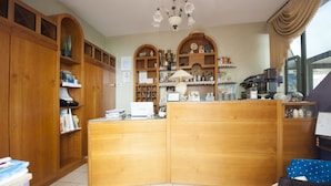 A cozy, well-organized room with wooden furniture, a coffee machine, and shelves filled with books and decorative items. - Hotel Athena (Spoleto)