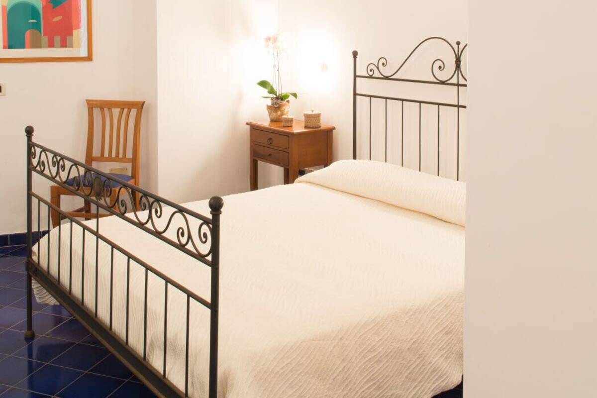Un dormitorio con cama, una silla, una mesita de noche y un cuadro en la pared.