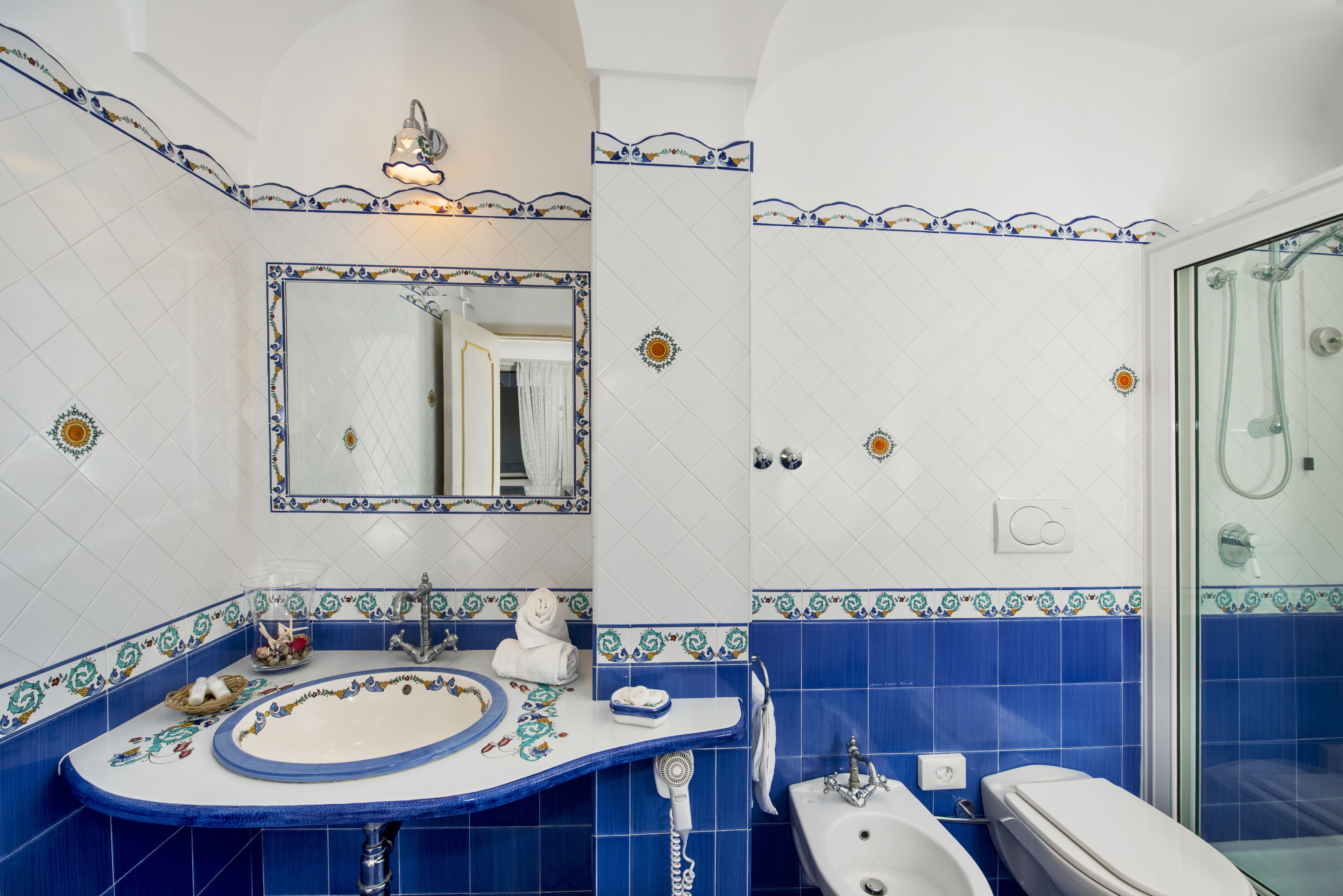 A bathroom with a white sink, blue tiles, a mirror, and a glass shower enclosure.
