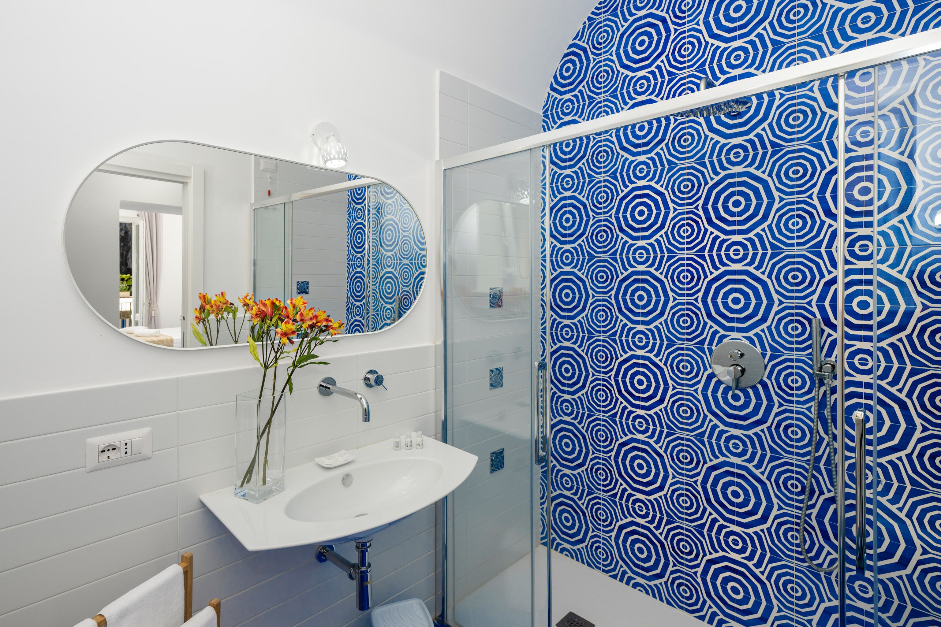 A bathroom with a white sink, a mirror, and a shower with blue patterned tiles.