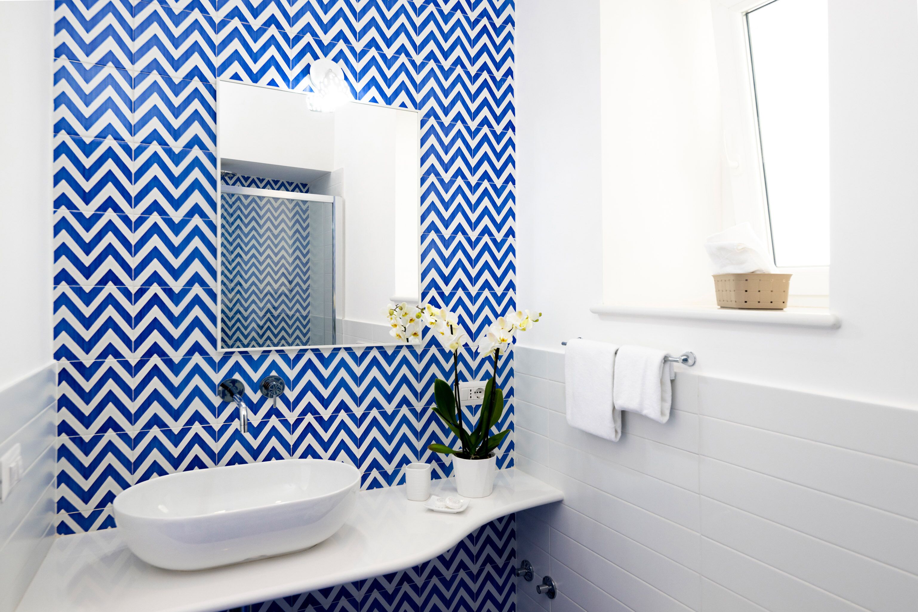 A bathroom with a white sink, a mirror, and a blue and white chevron-patterned wall.