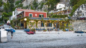A seaside restaurant with outdoor seating, a stone wall, and boats in the foreground. - Alfonso a Mare (Furore)