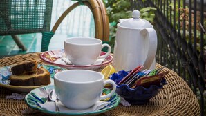 A balcony with a wicker table set for tea, a chair, and a view of a cliff and greenery. - Alfonso a Mare (Furore)