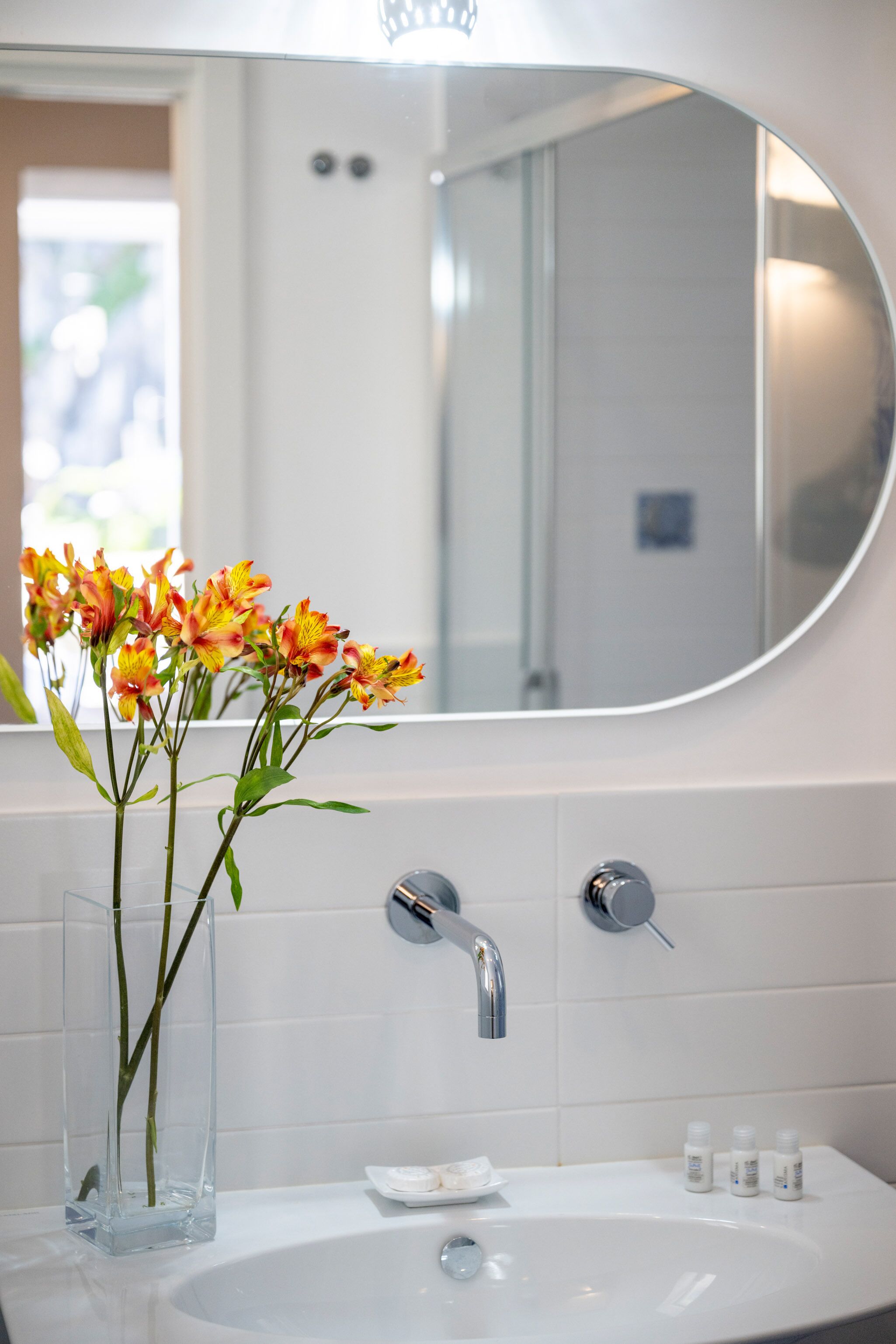 A bathroom with a white sink, a mirror, and a vase with flowers.
