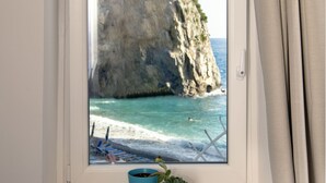 A window with a view of a rocky coastline, a small plant on the windowsill, and a curtain partially drawn. - Alfonso a Mare (Furore)