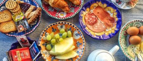 A breakfast spread with croissants, ham, eggs, and fruit on a table.