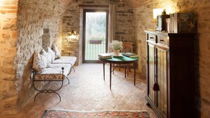 A cozy room with a brick ceiling, stone walls, a wooden bench, a table with chairs, and a cabinet. - Hotel Tenuta di Canonica (Todi)