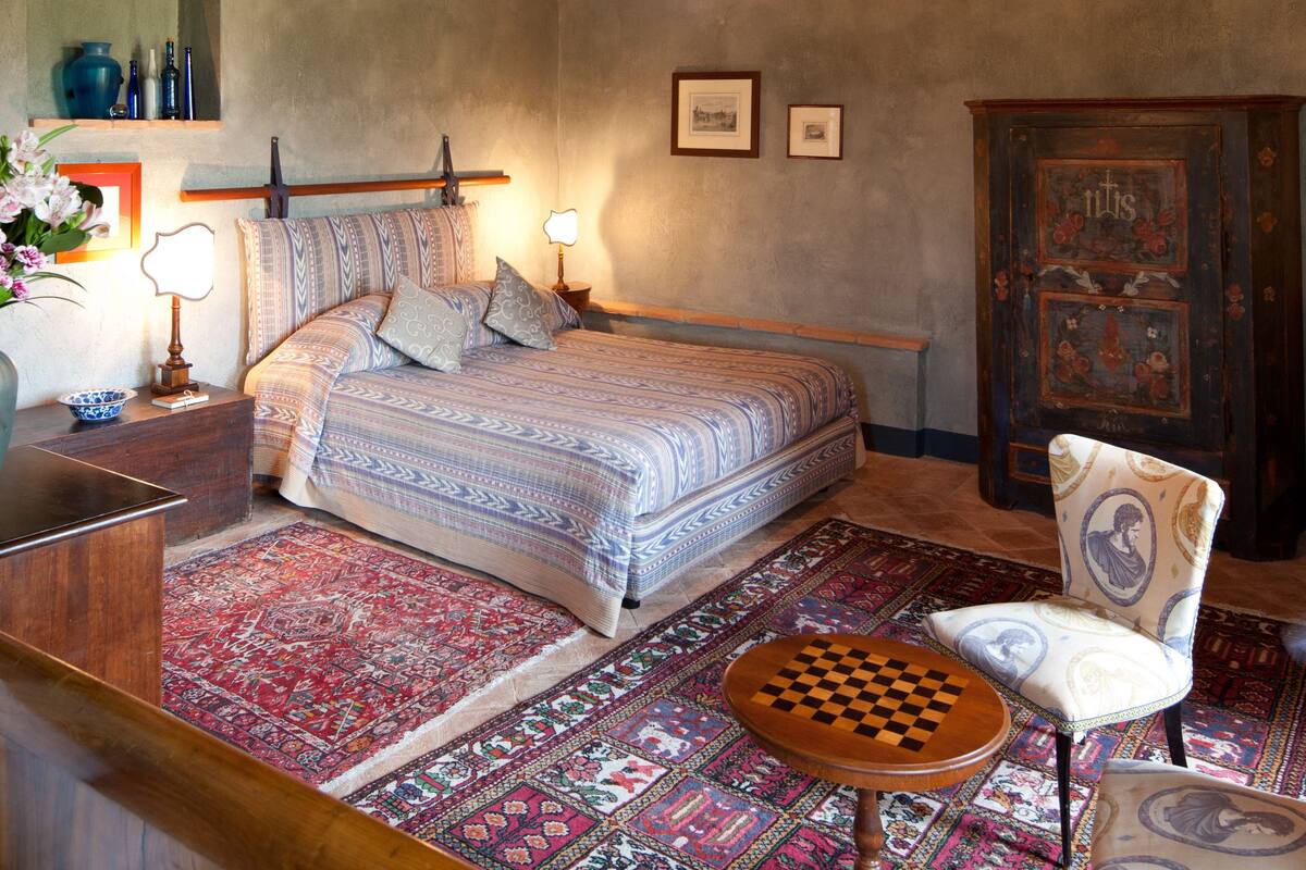 A bedroom with a bed, bedside table, lamp, chair, and a checkered table.