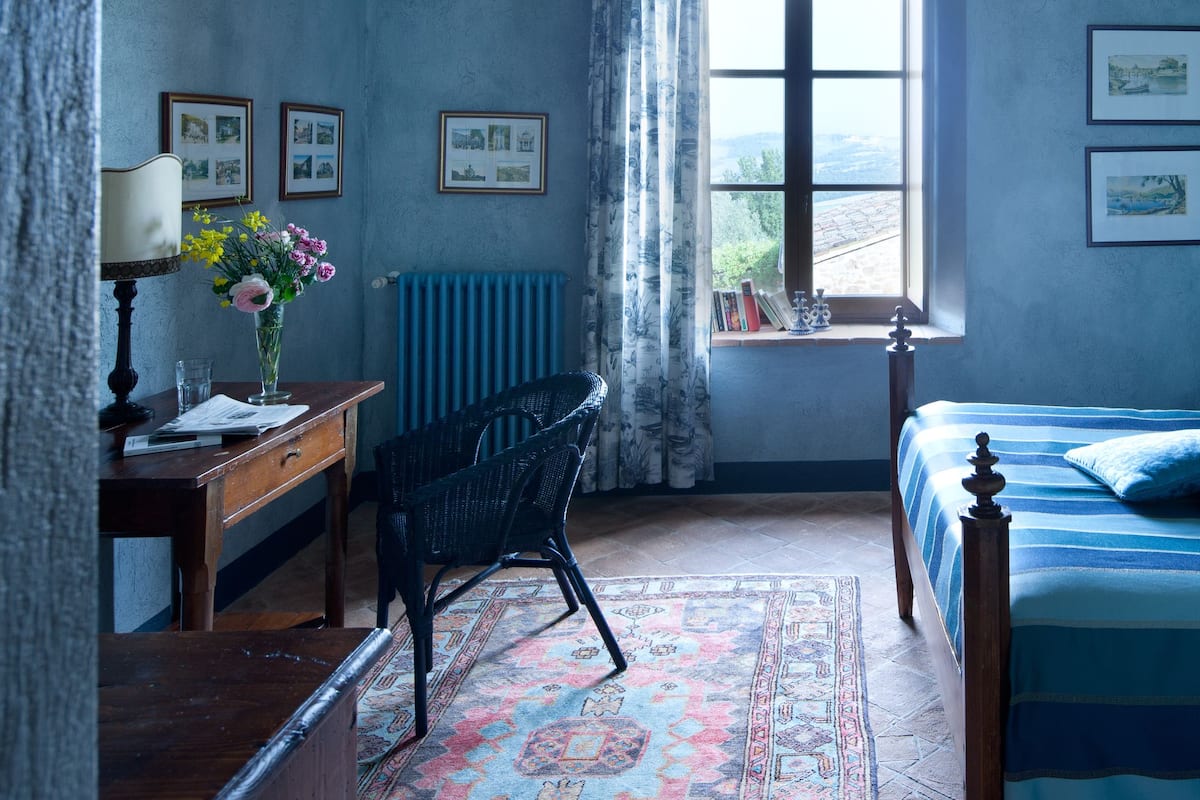 A bedroom with a bed, a desk, a chair, a window, and a radiator.