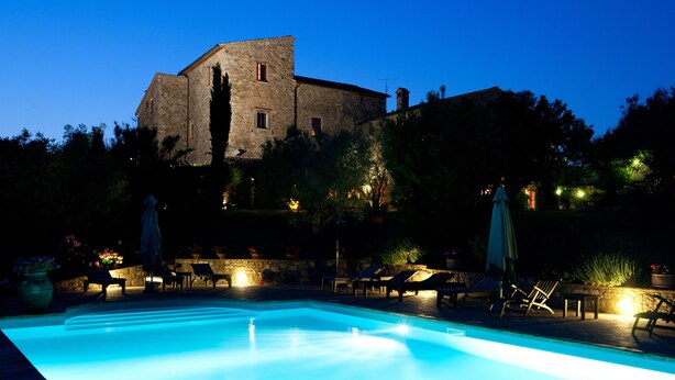 A swimming pool with lounge chairs and umbrellas, surrounded by stone walls and trees. - Hotel Tenuta di Canonica (Todi)