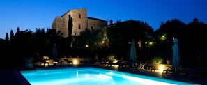 Une piscine entourée de murs de pierre et d’arbres, avec des chaises longues et des parasols.