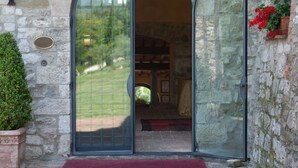 A stone building entrance with a glass door, a red mat, and a potted plant. - Hotel Tenuta di Canonica (Todi)