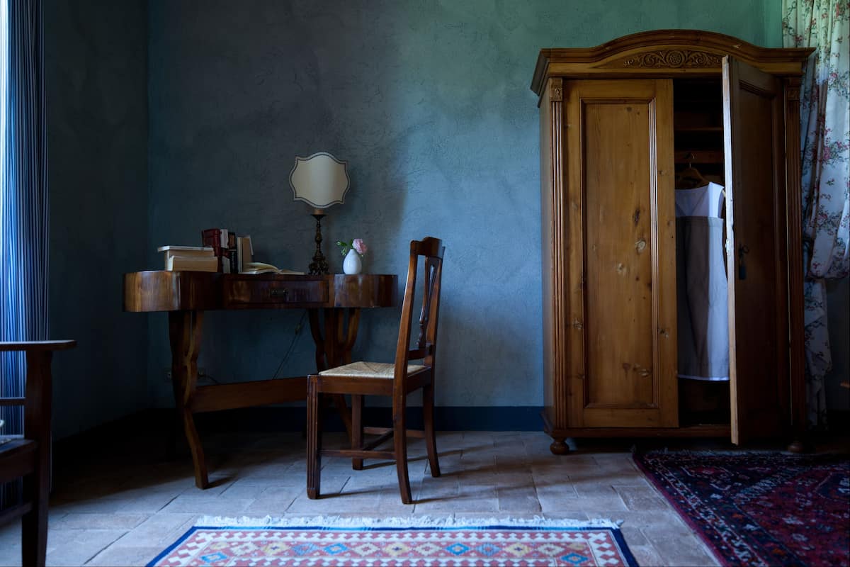 A room with a wooden table, a chair, a wooden wardrobe, and a patterned rug.
