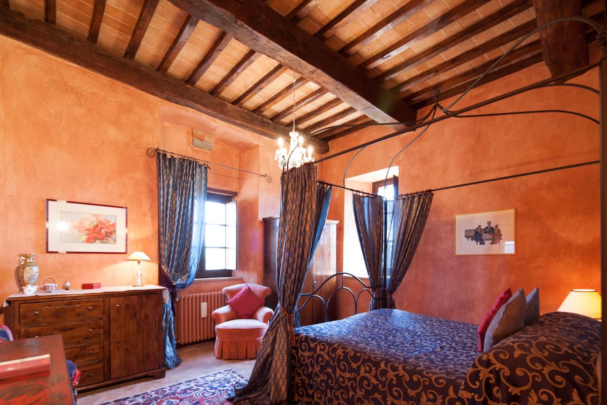 A bedroom with a canopy bed, wooden ceiling beams, a radiator, and a dresser.