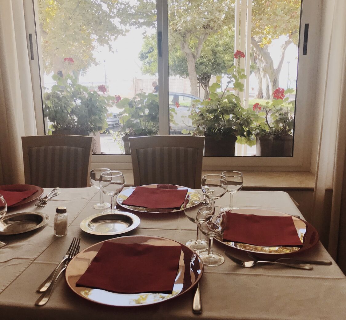 Une table à manger dressée pour quatre personnes, avec vue sur un jardin par la fenêtre.