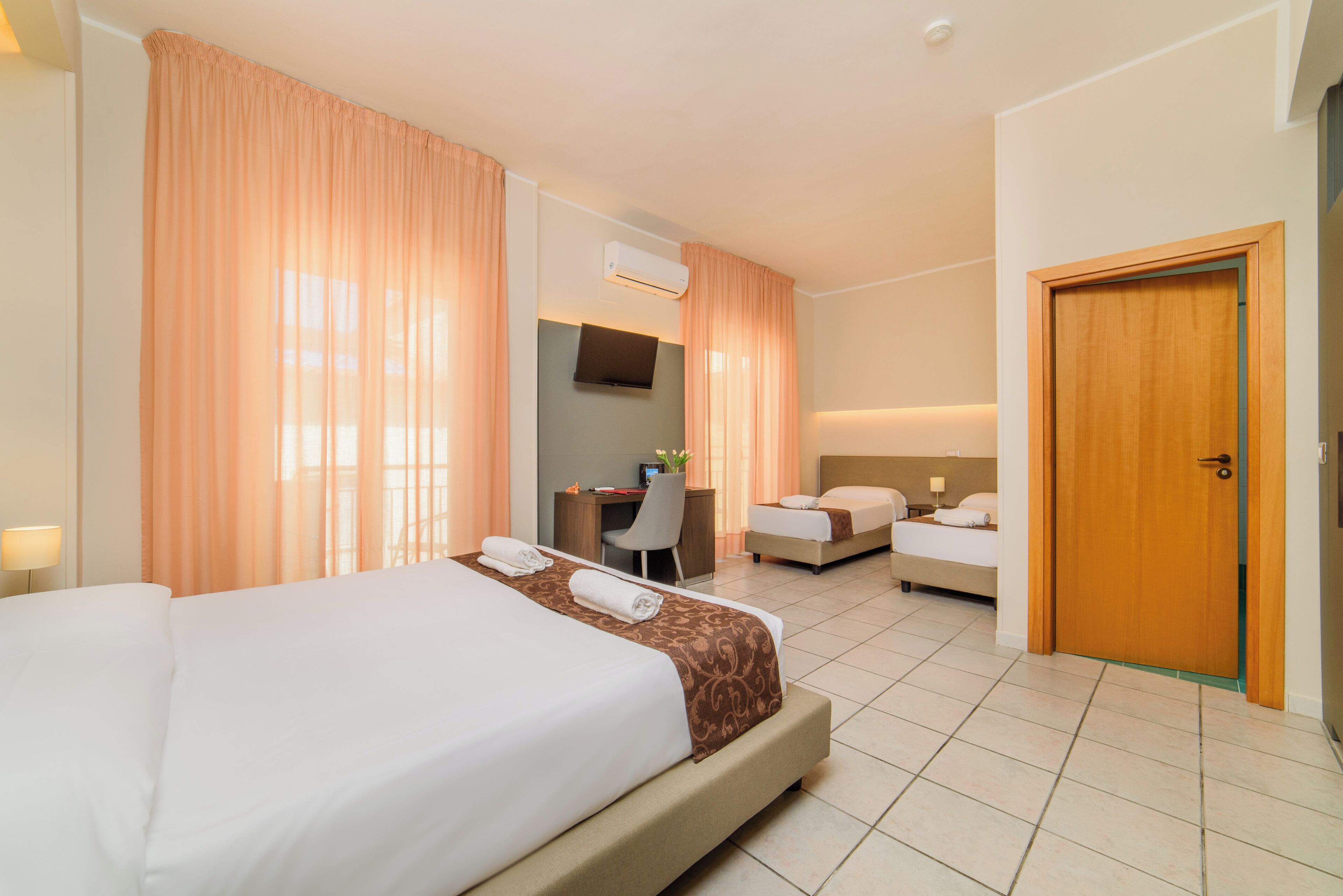 Een hotelkamer met een groot bed, een bureau, een tweede bed en een deur.