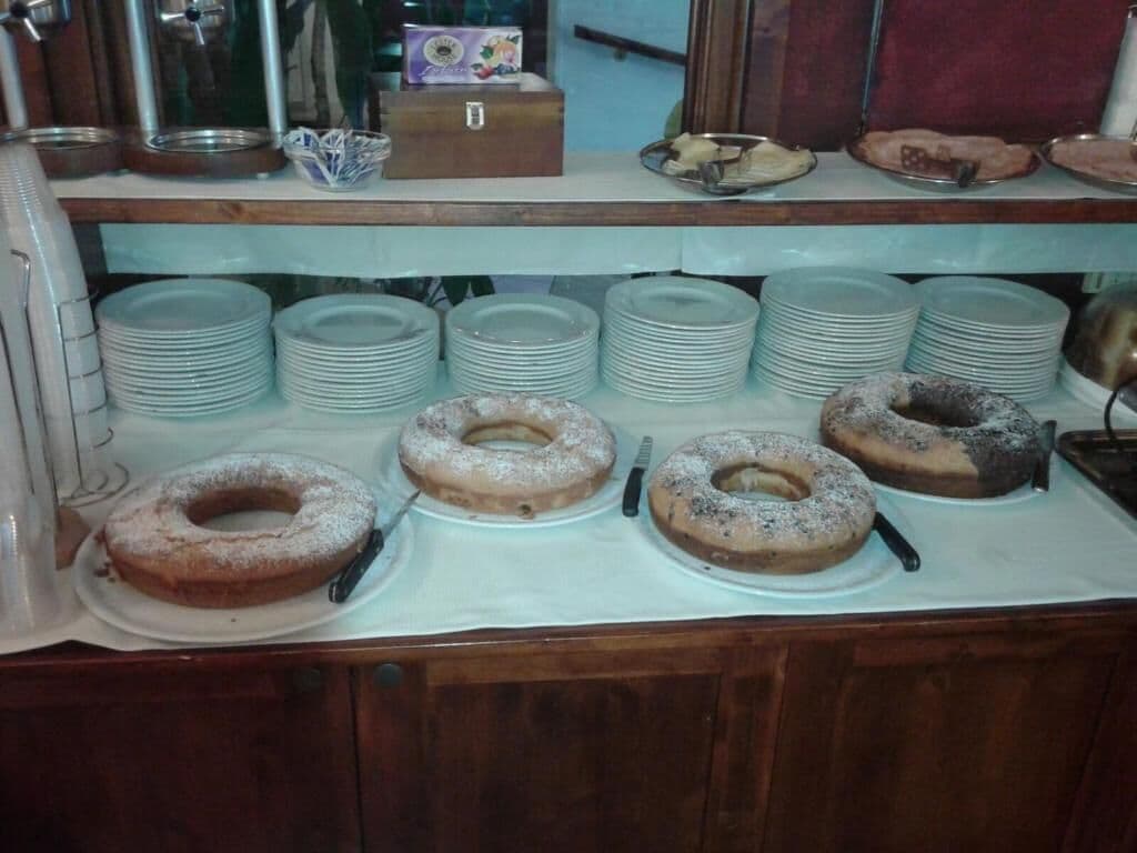 Un mostrador de buffet con múltiples platos apilados en estantes y varias pastas con forma de anillo sobre platos.