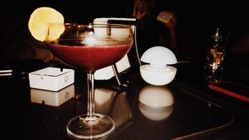 Ein Cocktail im Glas mit Zitronenscheibe, ein weißes Servietttuch und eine kleine weiße Schale mit einem Löffel auf dunklem Untergrund.