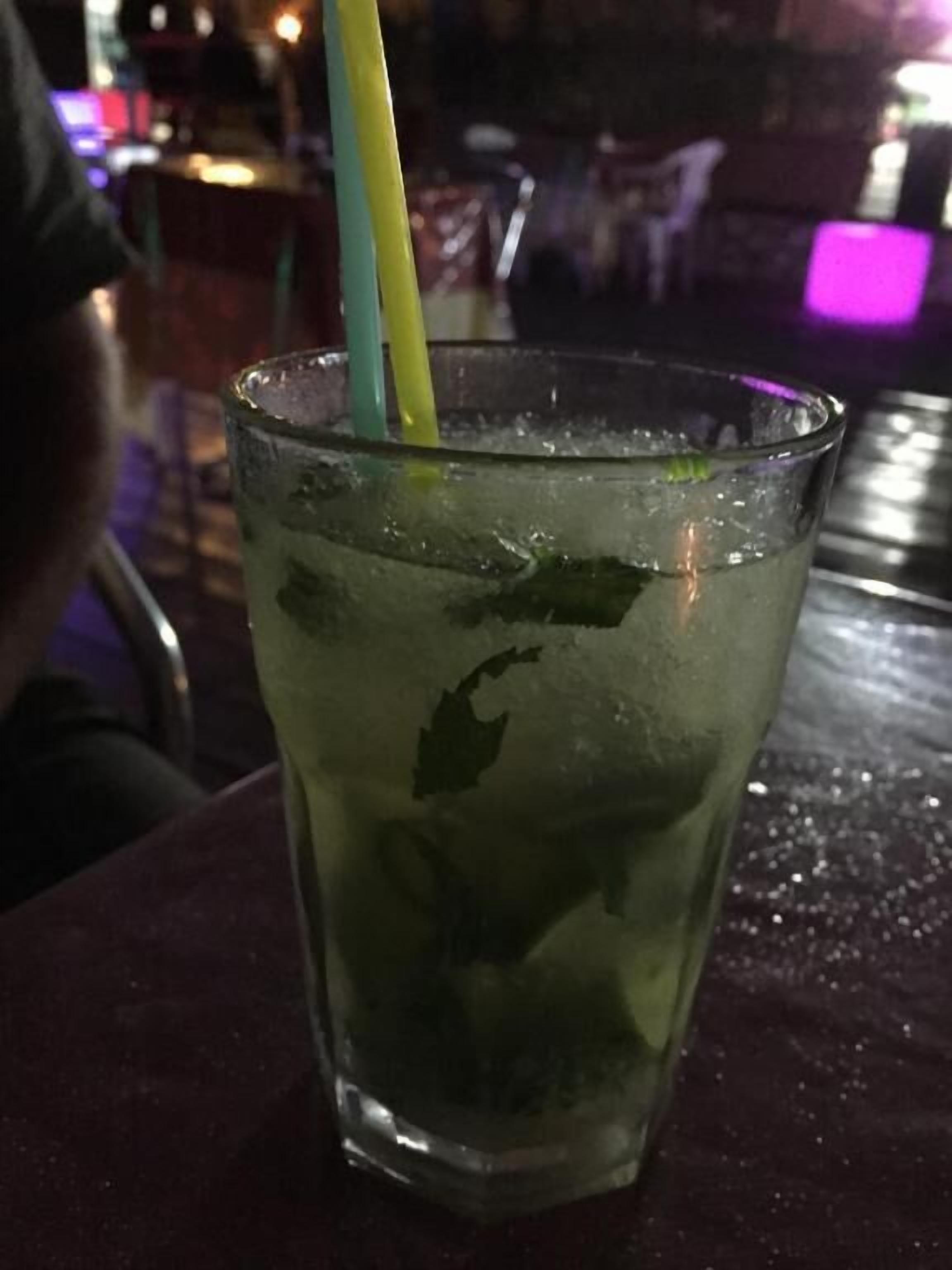 A glass of iced beverage with a straw, containing mint leaves, on a table.