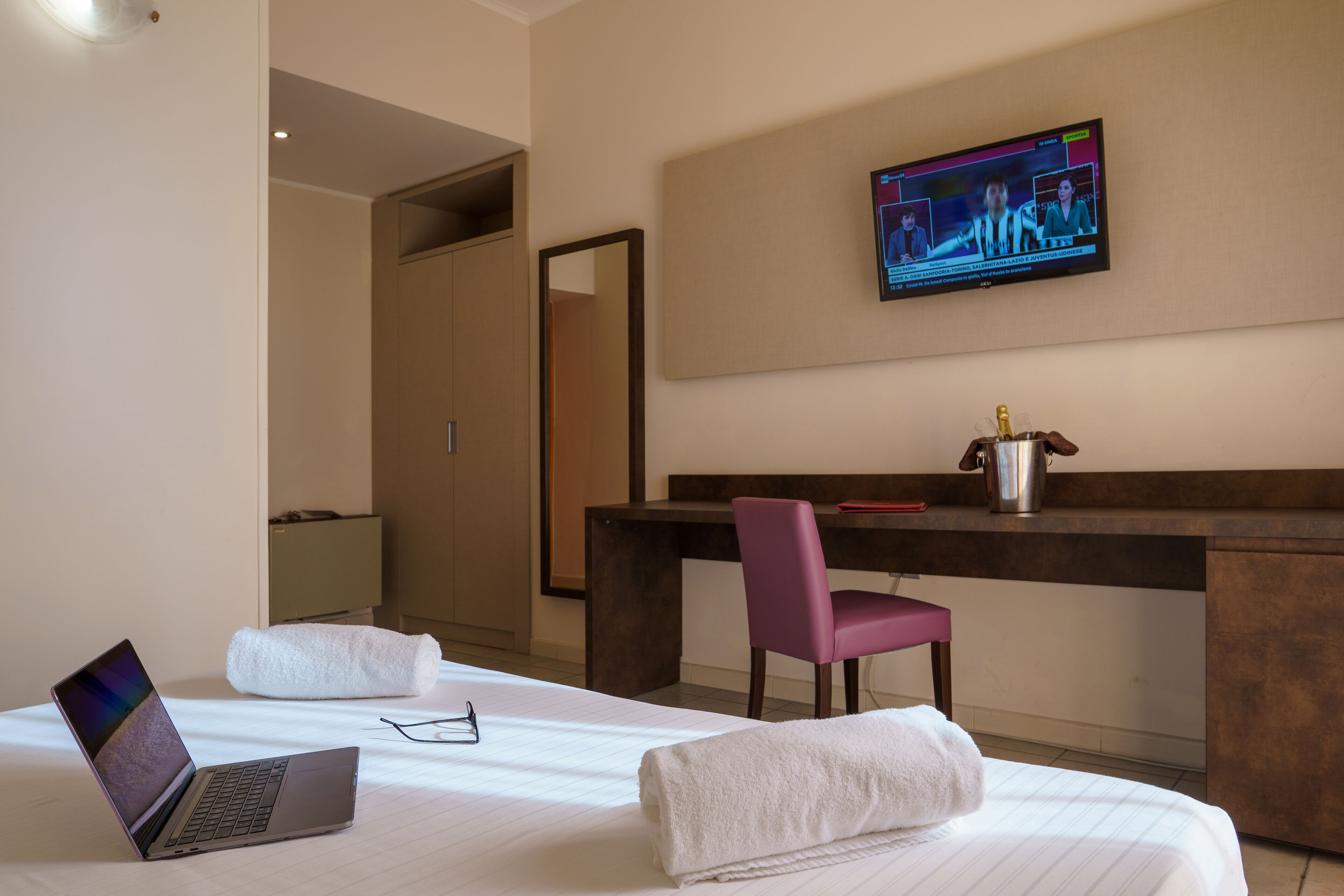 A hotel room with a bed, a desk, a laptop, a TV, and a chair.