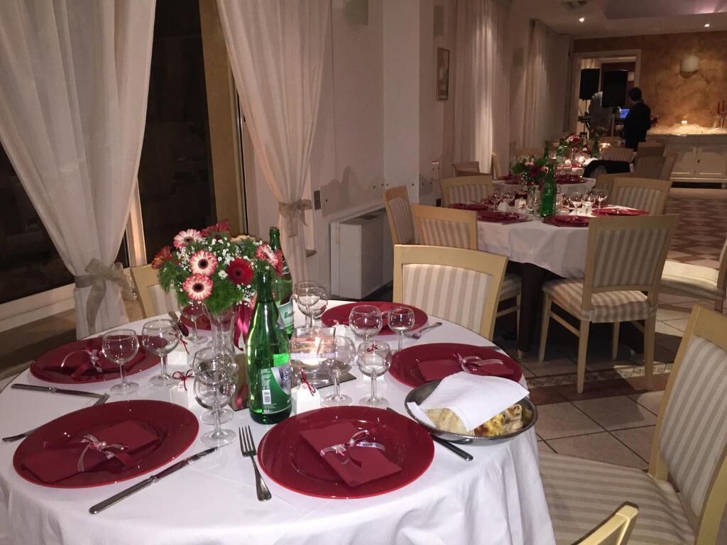 Zona pranzo con tavoli rotondi apparecchiati per un pasto, con tovaglie bianche, tovaglioli rossi e bicchieri.