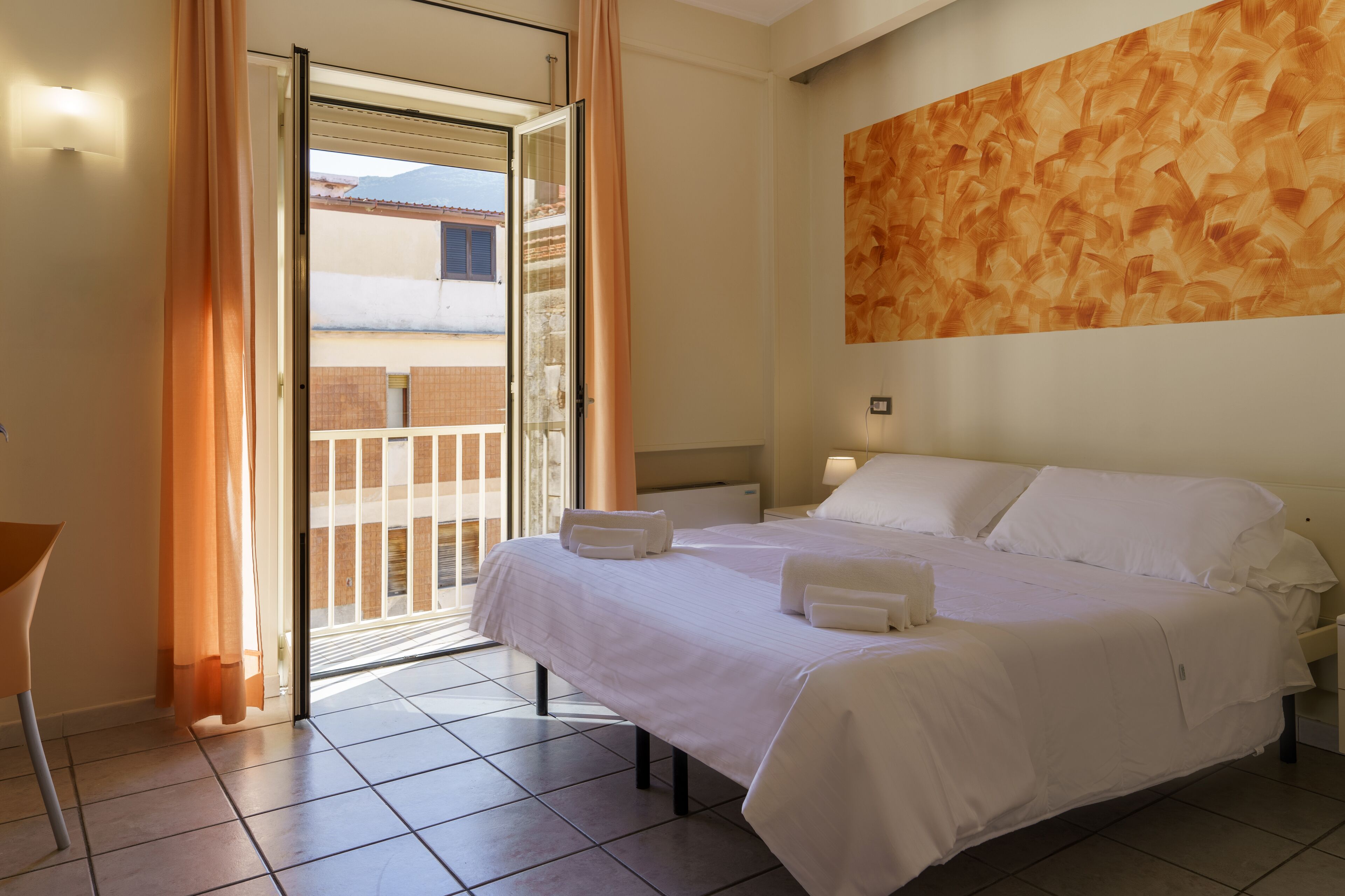Une chambre d’hôtel comprenant un lit, une chaise, une table de chevet et donnant sur un espace extérieur grâce à une porte vitrée.