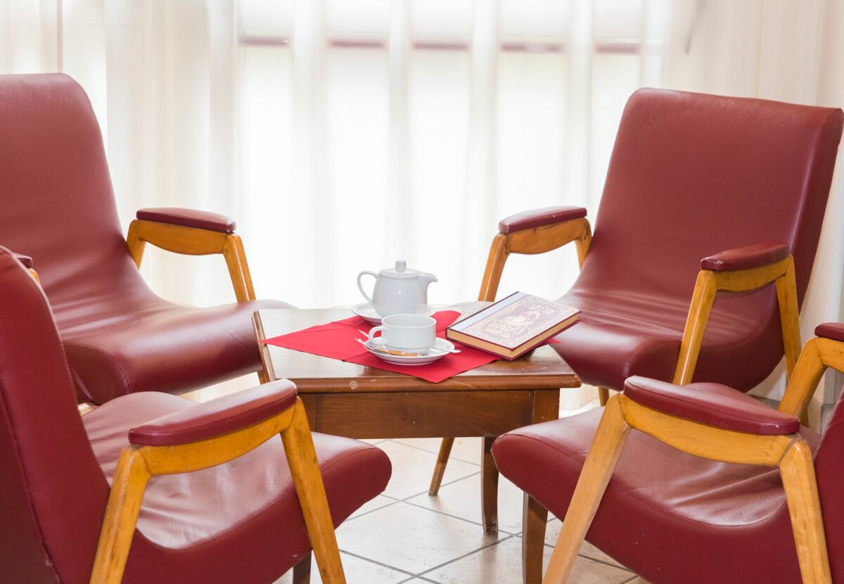 A room with four red leather chairs around a wooden table, a white teapot, a cup, and a book.
