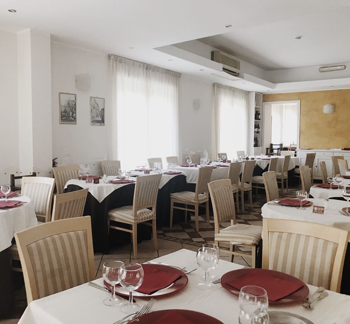 Zona pranzo con diversi tavoli apparecchiati per un pasto, caratterizzata da sedie a righe e tovaglioli rossi.