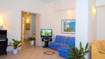 A living room with a sofa, a television, a piano, and potted plants.