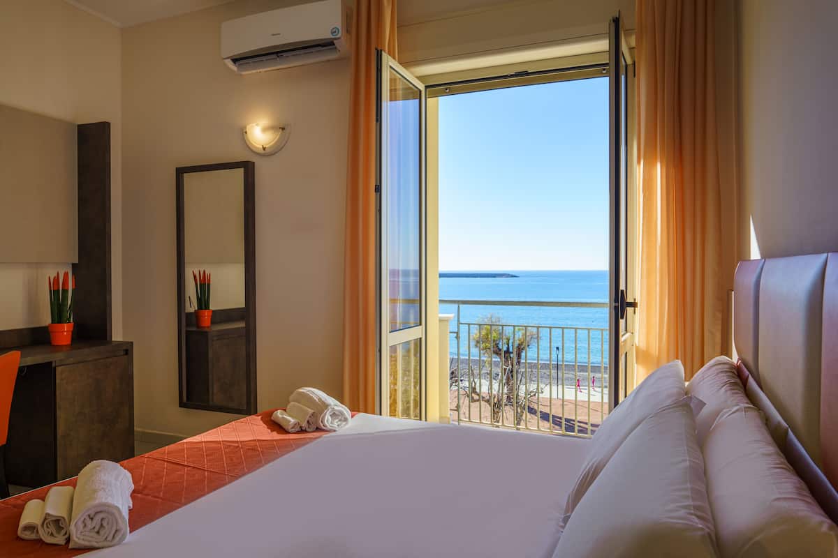 A hotel room with a bed, a desk, a mirror, and a view of the beach.