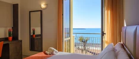 A hotel room with a bed, a desk, a mirror, and a view of the beach.