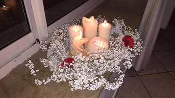 A candle arrangement with white flowers and a red rose on a tiled floor near a window.