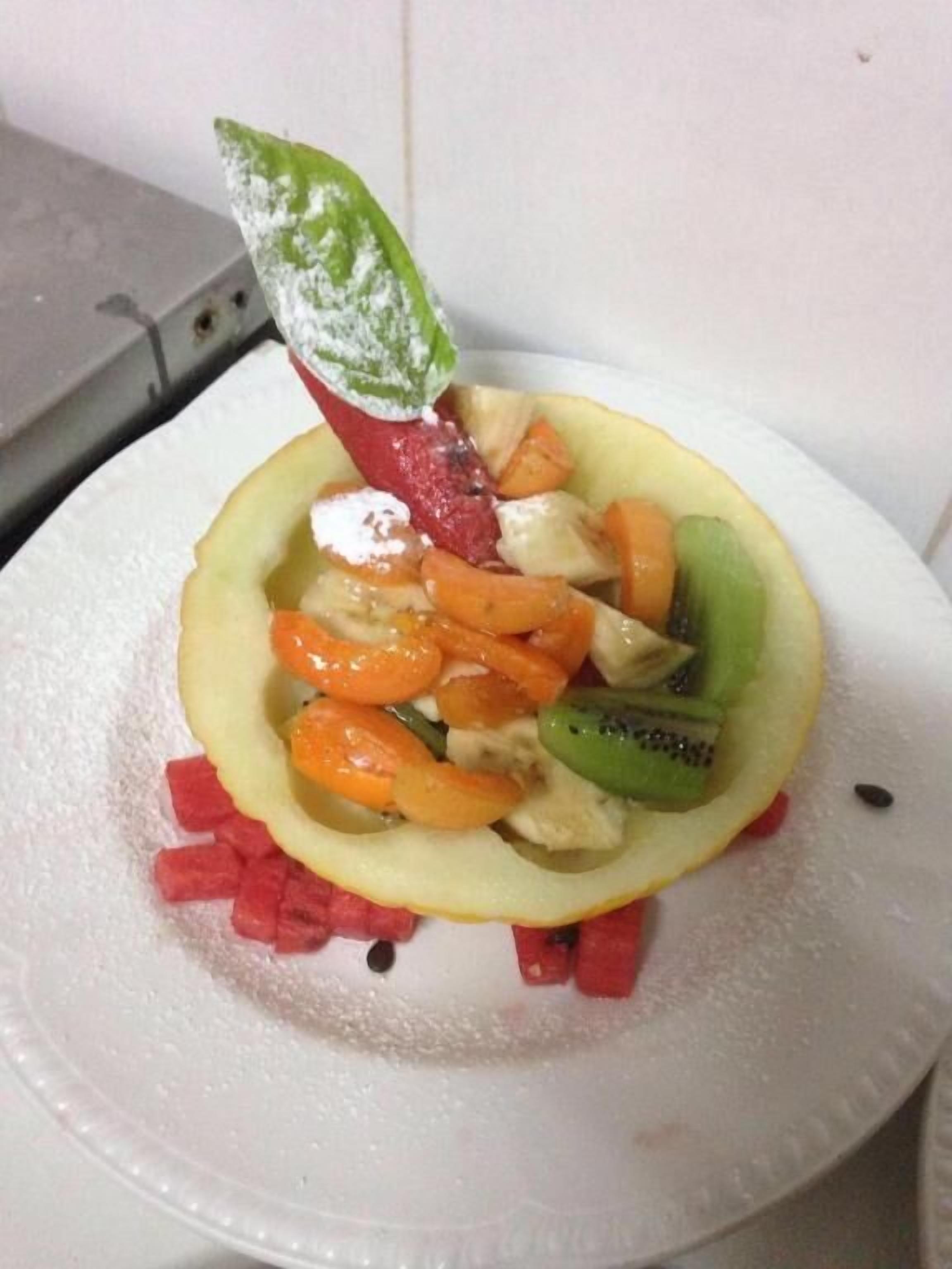 Une salade de fruits servie dans un bol en papier, décorée d’une feuille.