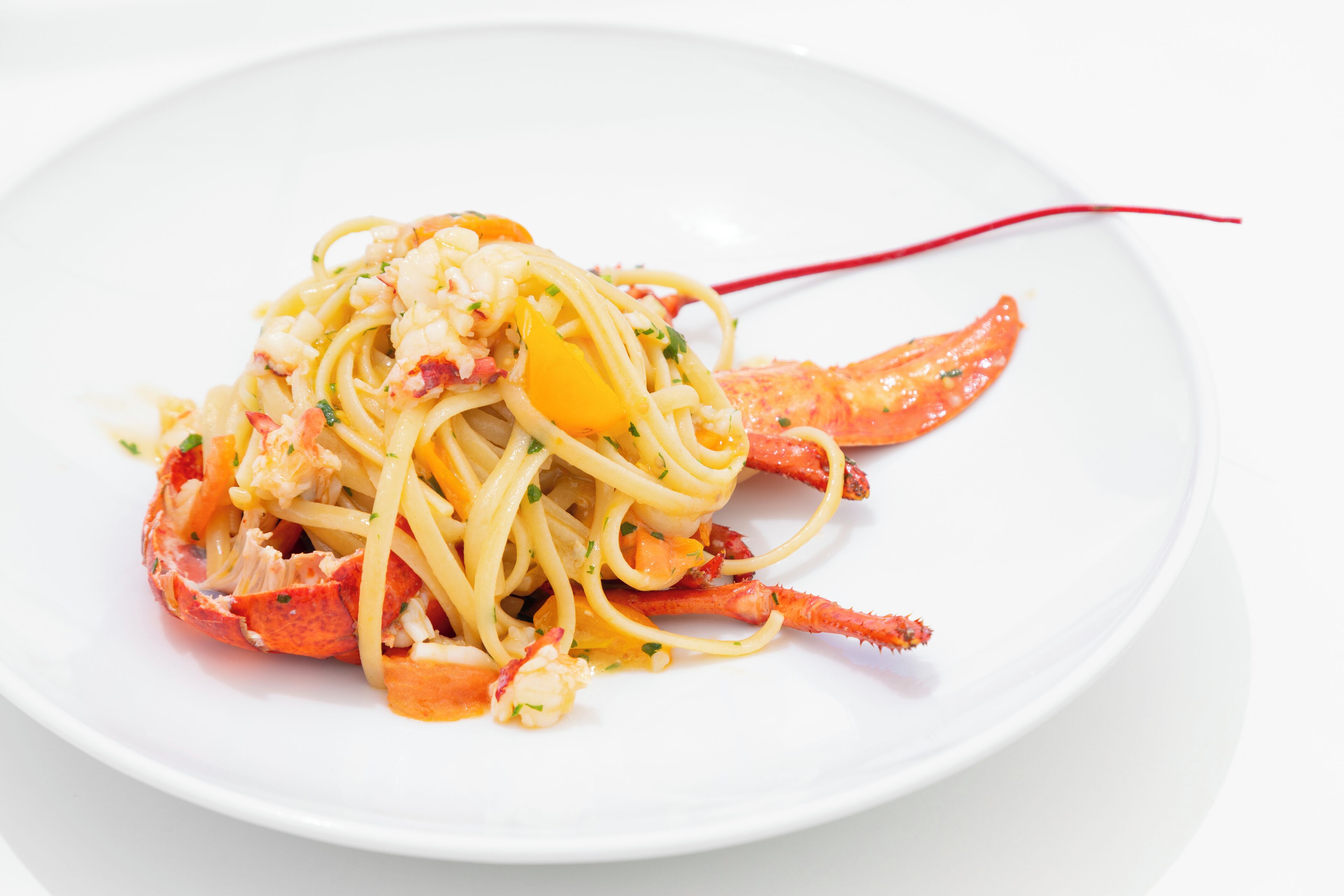 Une assiette de spaghettis accompagnée de queues de homard et de tranches de citron.