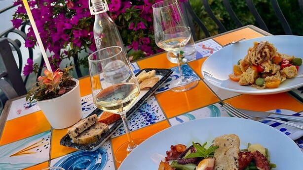 A table set with plates of food, glasses of wine, and a potted plant, overlooking a scenic view. - Albergo Diffuso Bacco Furore (Furore)
