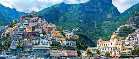A coastal town with colorful buildings, a beach, and mountains in the background.