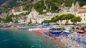 A coastal town with a beach crowded with people, a boat docked near the shore, and buildings with a mix of architectural styles. - Albergo Diffuso Bacco Furore (Furore)