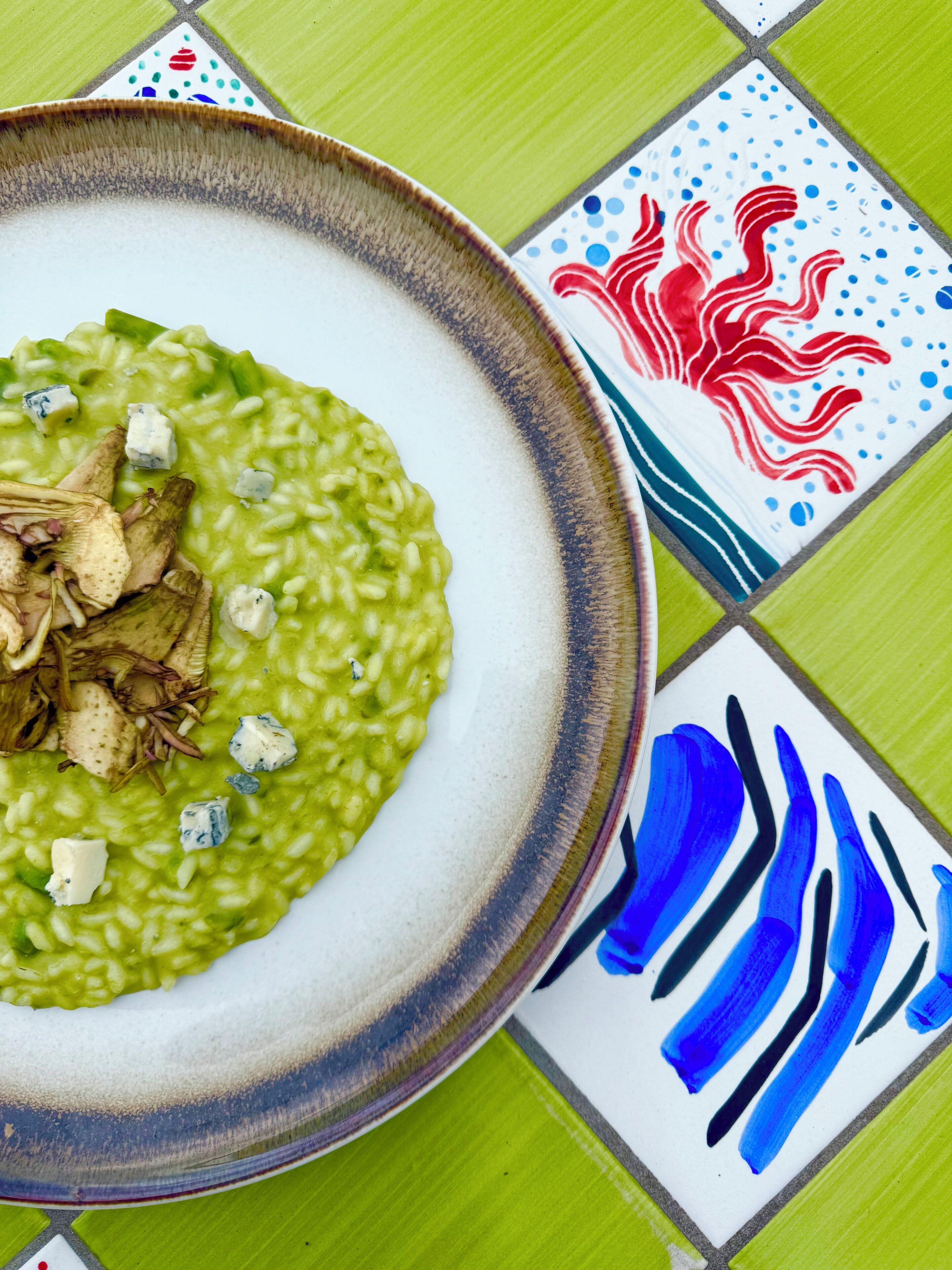 Een schaal groene risotto met paddenstoelen en blauwe kaas op een geruit tafelkleed.