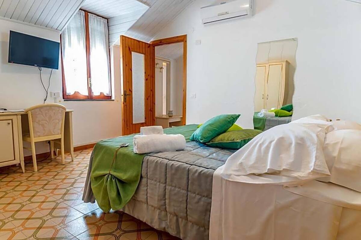 A bedroom with a bed, a desk, a chair, a television, and a mirror.