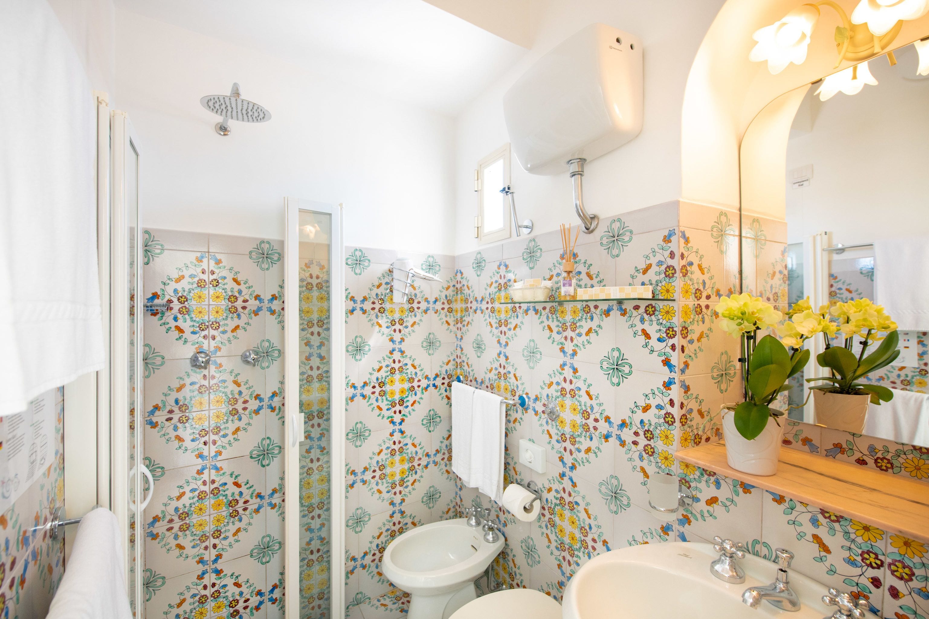 Ein Badezimmer mit Dusche, Bidet, Waschbecken und einem Spiegel mit Blumenmuster-Fliesen.