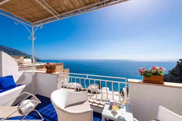 A balcony with white wicker furniture, a glass table, and potted flowers. - Casa Guadagno (Positano)
