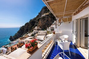 A balcony with a view of the sea, white wicker furniture, and potted plants. - Casa Guadagno (Positano)
