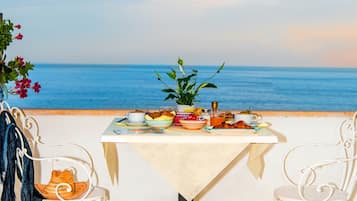 A table set for two with a view of the sea, a patterned floor, and white chairs.