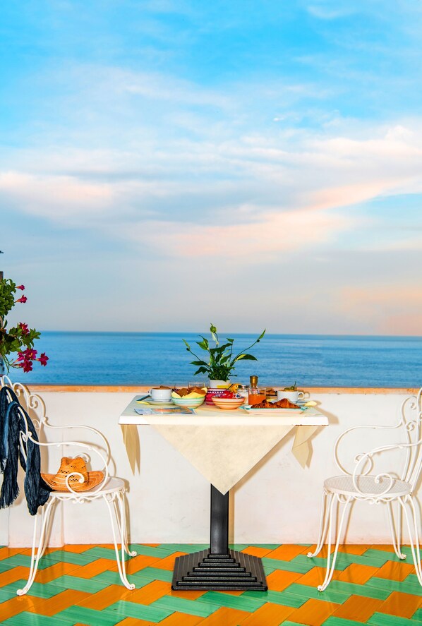 Una mesa para dos con vistas al mar, un suelo estampado y sillas blancas.
