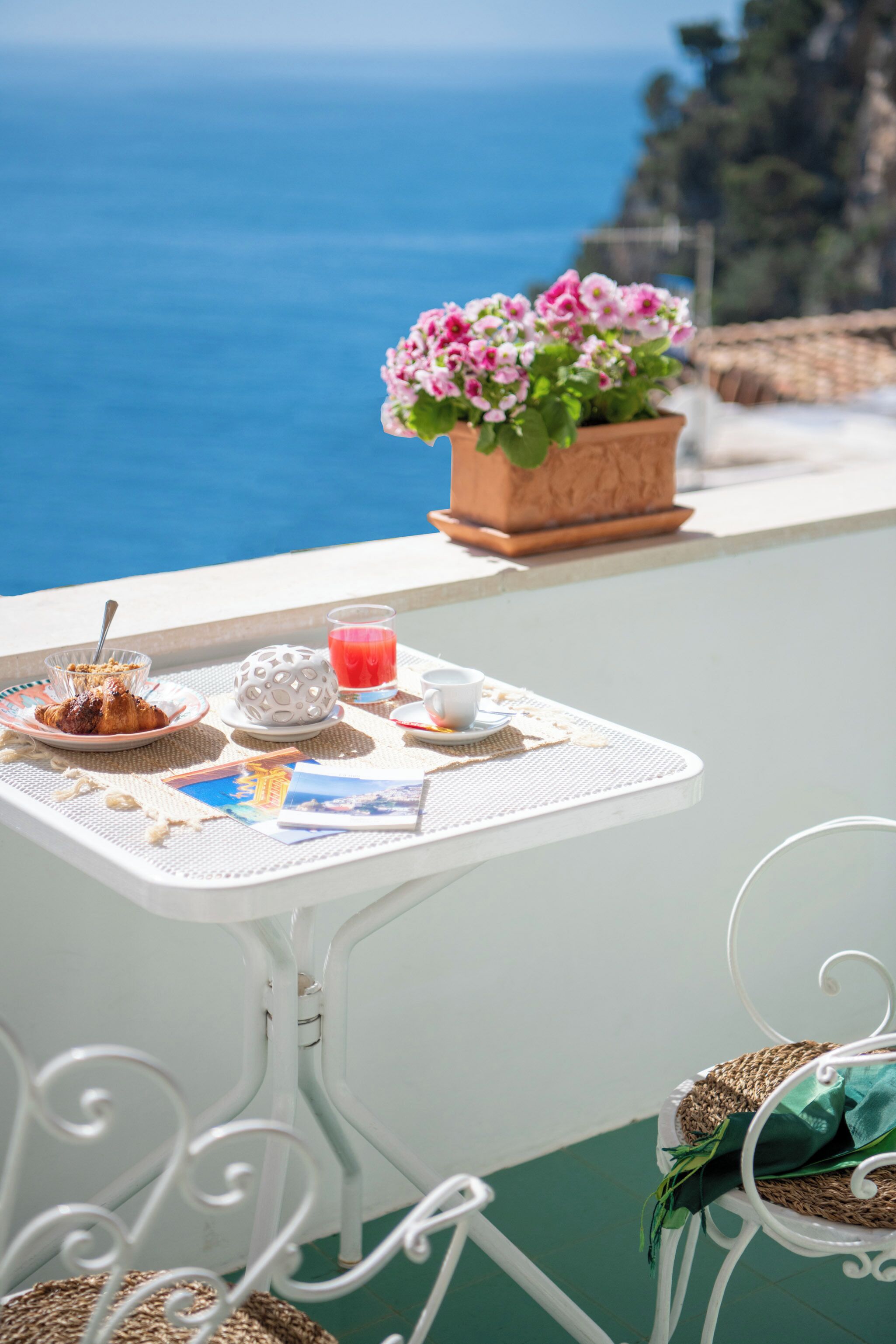 A table with breakfast items, a potted plant, and a view of the sea.