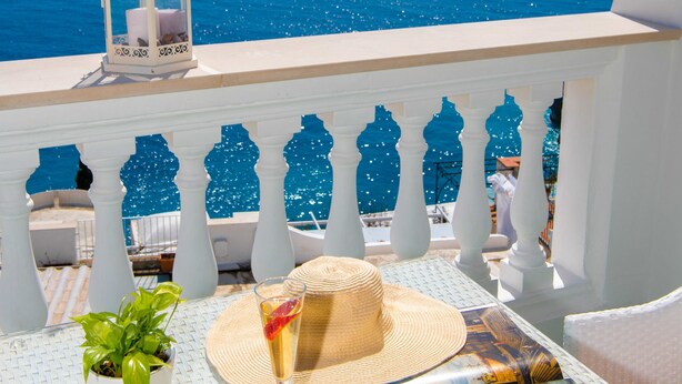 A balcony with a view of the sea, a table with a plant, a straw hat, a glass of drink, and a magazine. - Casa Guadagno (Positano)