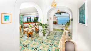 A bright dining area with a view of the sea, white walls, and colorful patterned floor tiles. - Casa Guadagno (Positano)