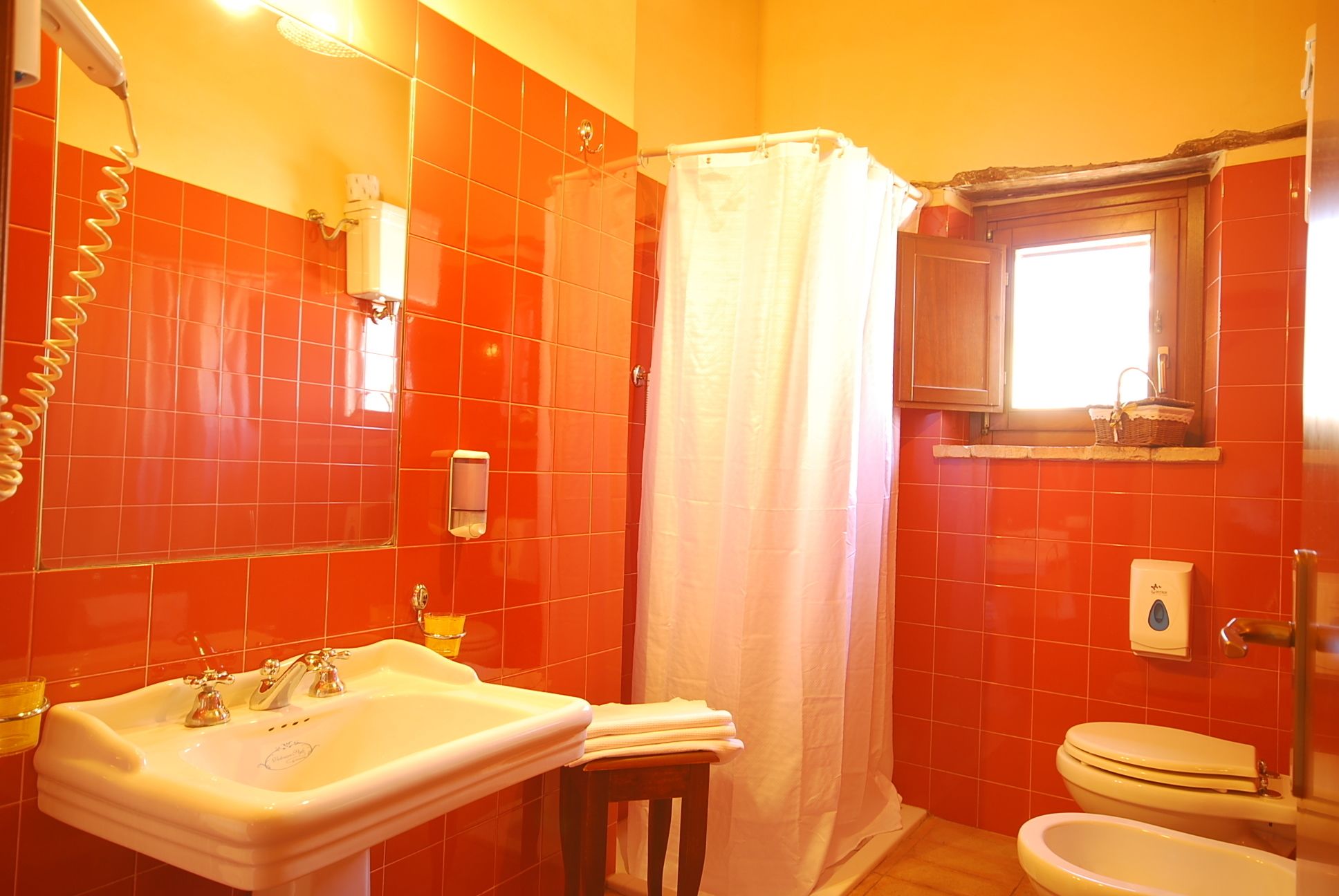 A bathroom with red tiles, a white sink, a toilet, and a shower curtain.