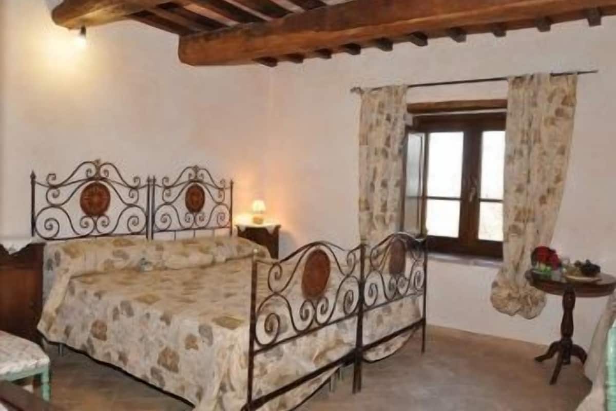 Une chambre à coucher avec un lit à motifs de pierre, un plafond en bois, une petite table de chevet avec une lampe et une fenêtre avec des rideaux.