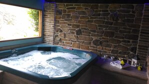Un bain à remous avec un mur en pierre en arrière-plan et une fenêtre.